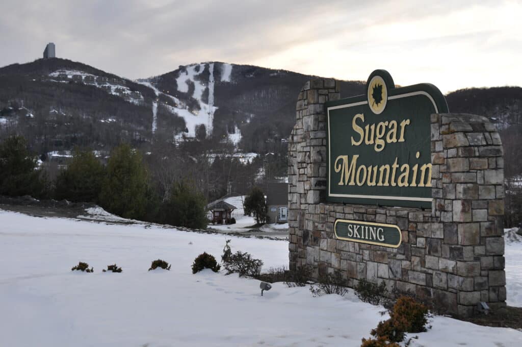 Sugar Mountain Skiing stone sign with snowy ski slopes behind